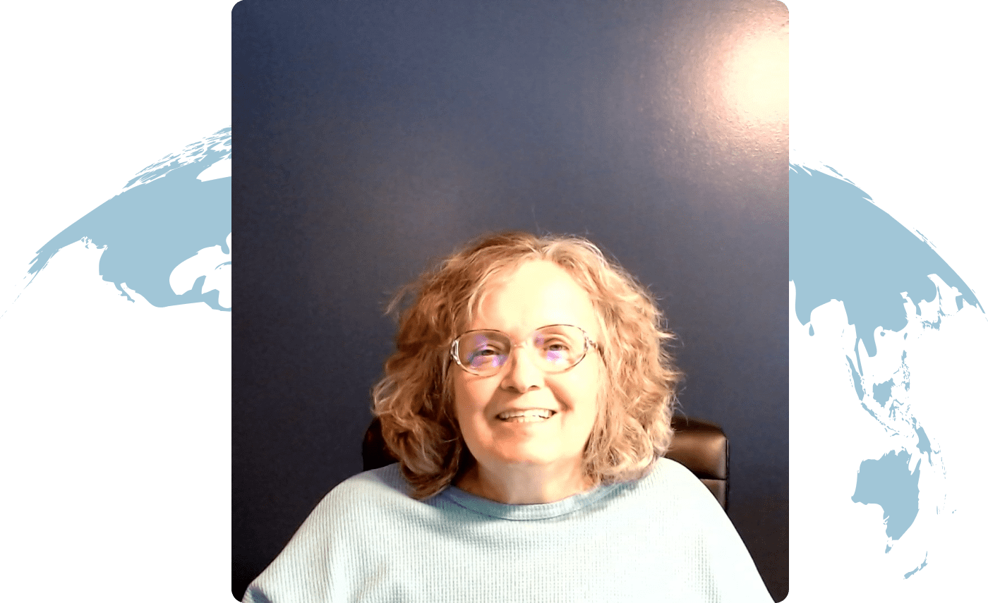 Smiling woman with glasses and curly hair in a cozy sweater.