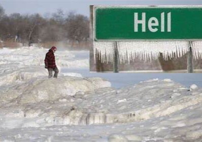 Person walking through deep snow near a Hell town sign.